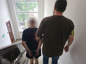 Zdjęcie przedstawia policjant Wydziału Kryminalnego, który prowadzi mężczyznę  w kajdankach po schodach.