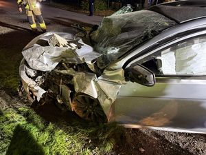 Zdjęcie przedstawia skutki wypadku drogowego- srebrny zniszczony pojazd w porze nocnej.