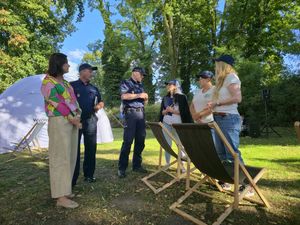 Na zdjęciach są przedstawieni seniorzy podczas spotkania z policjantami.  Spotkanie jest w parku, seniorzy siedzą przy stolikach.