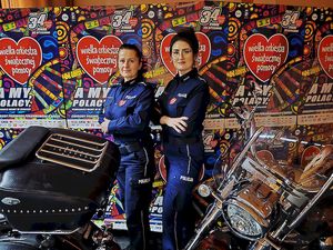 Policjantki na tle ścianki z plakatami Wielkiej Orkiestry Świątecznej Pomocy