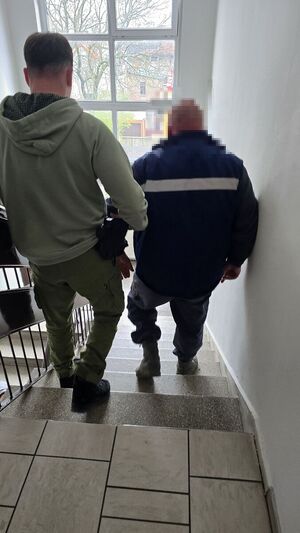 Funkcjonariusz Wydziału Kryminalnego prowadzi zatrzymanego po schodach